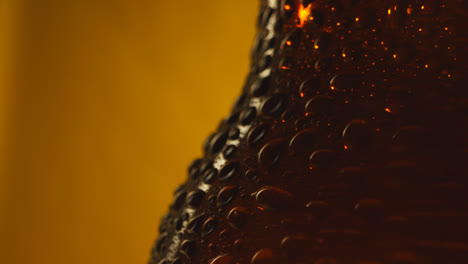 Macro-Shot-Of-Condensation-Droplets-On-Revolving-Bottle-Of-Cold-Beer-Or-Soft-Drinks-Against-Yellow-Background
